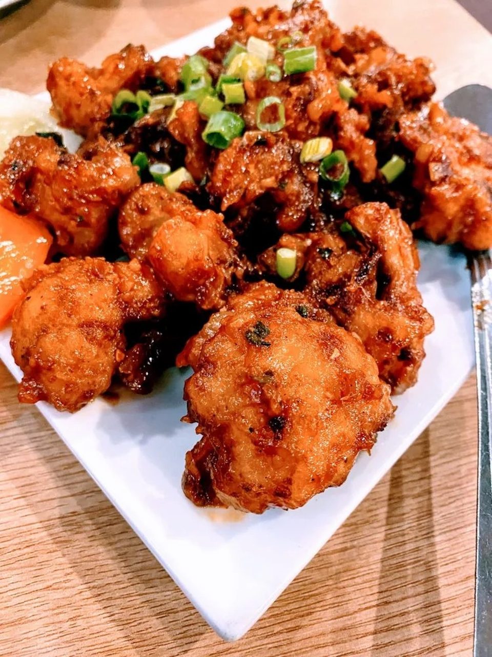 Crispy fried chicken pieces coated in a dark sauce and garnished with chopped green onions.