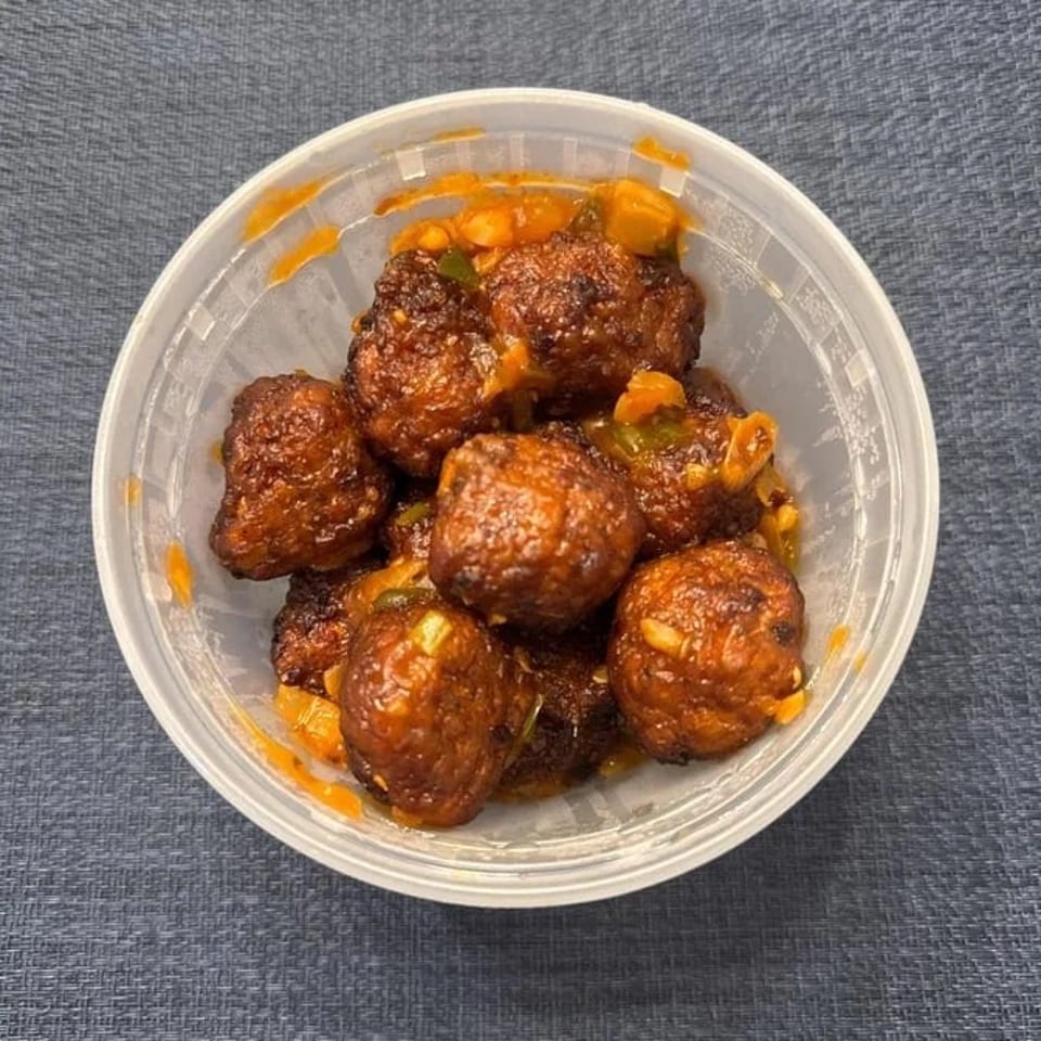 Close-up of Manchurian vegetable balls in a clear plastic container, coated in a rich, dark sauce.