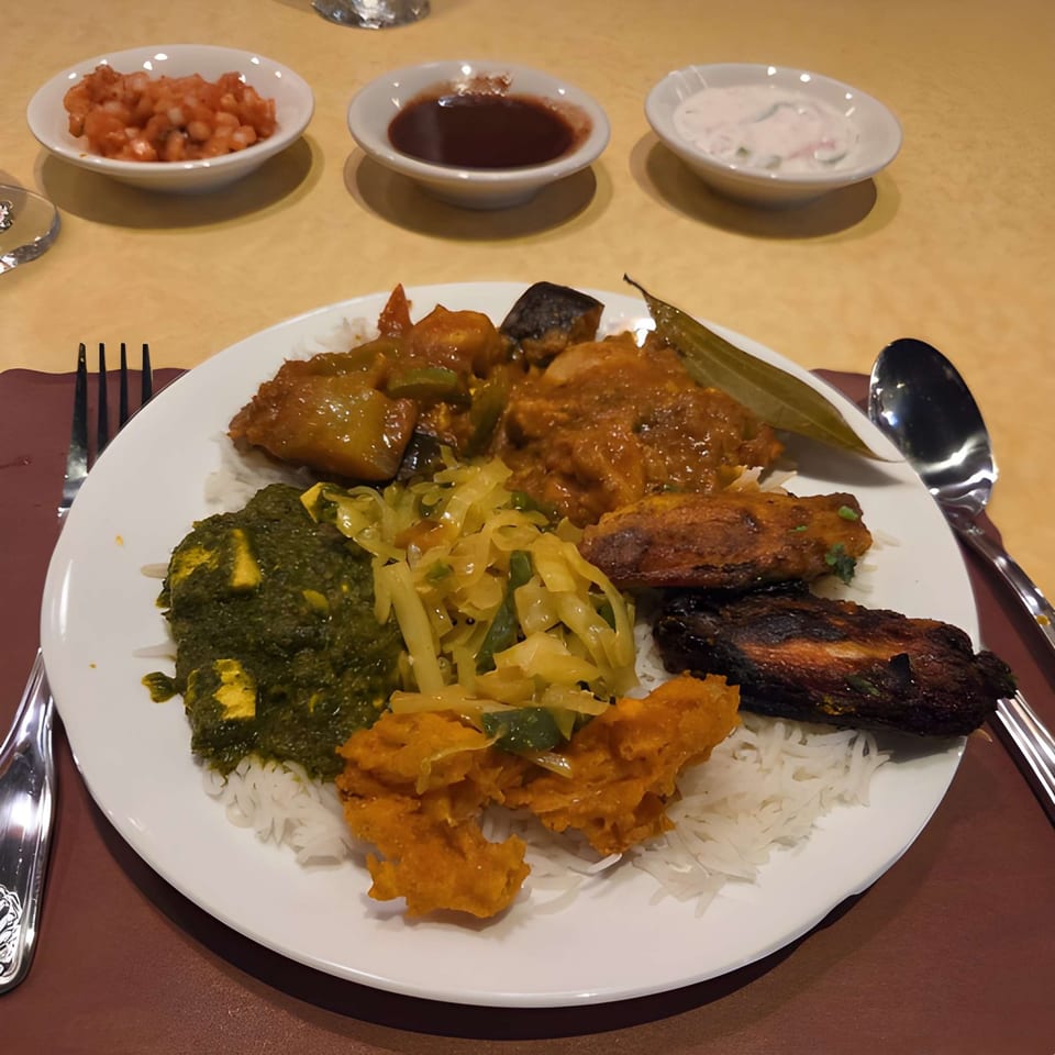 A white plate with various Indian dishes, including rice, curries, and fried items, with side sauces.