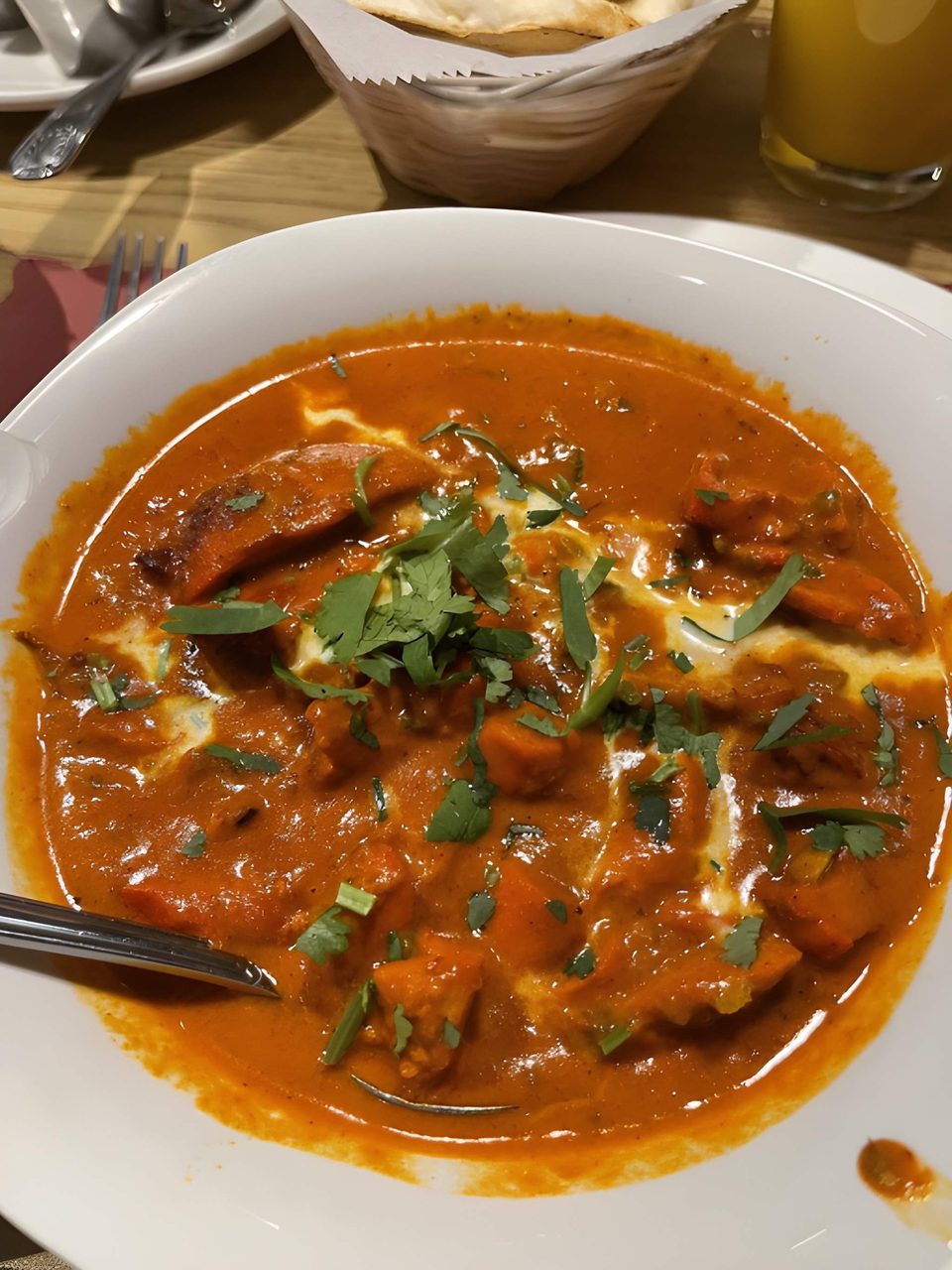 Close-up of a bowl of chicken tikka masala, garnished with cilantro and a swirl of cream.