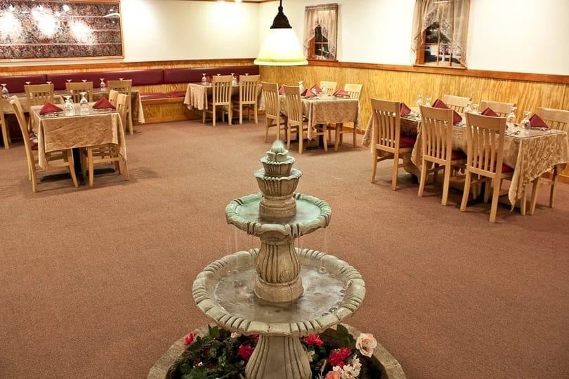 Restaurant dining room with a central fountain, tables with tablecloths, and wooden chairs.