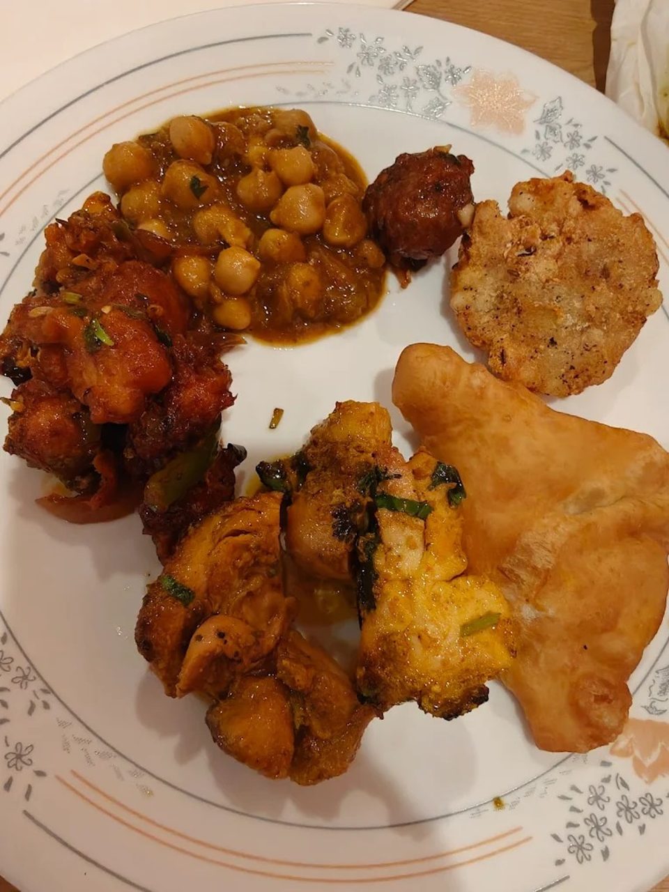 A white plate filled with various Indian dishes including chickpea curry, fried chicken, and flatbread.